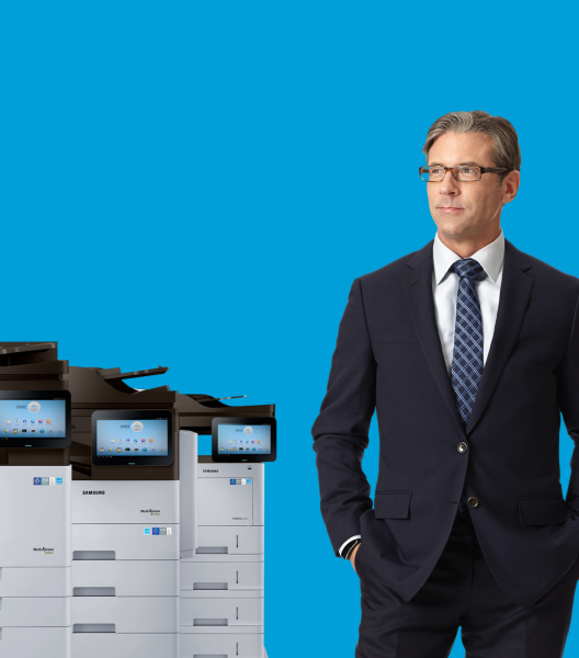 하늘색 배경에 정장을 입은 남성이 복합기 여러대 옆으로 서 있는 모습