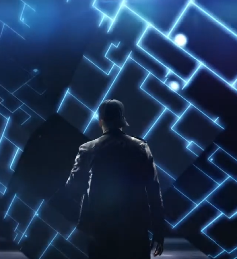 어두운 공간에서 한 남성 래퍼가 등을 보인 채 서 있다. 주변에는 푸른 빛의 선과 기하학적 패턴이 벽과 공간을 따라 빛나며 미래적인 분위기를 만든다. 남성은 재킷을 입고 있으며, 빛나는 디지털 구조물을 바라보고 있는 장면이다.
